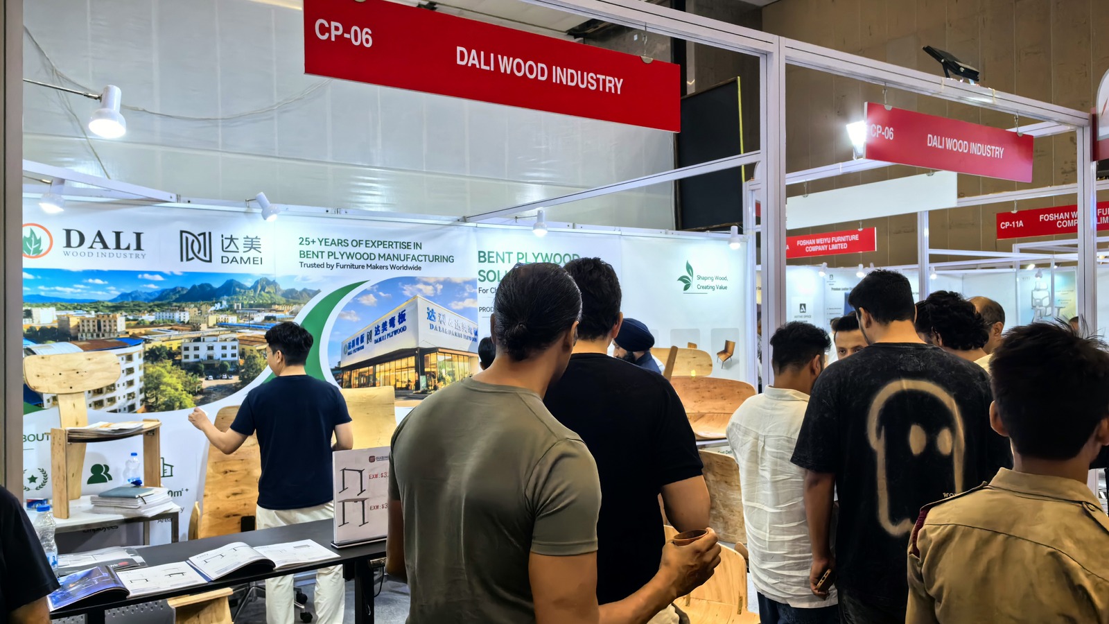 Visitors gathering around real bent plywood chair shells and furniture components at DALI Booth CP-06.